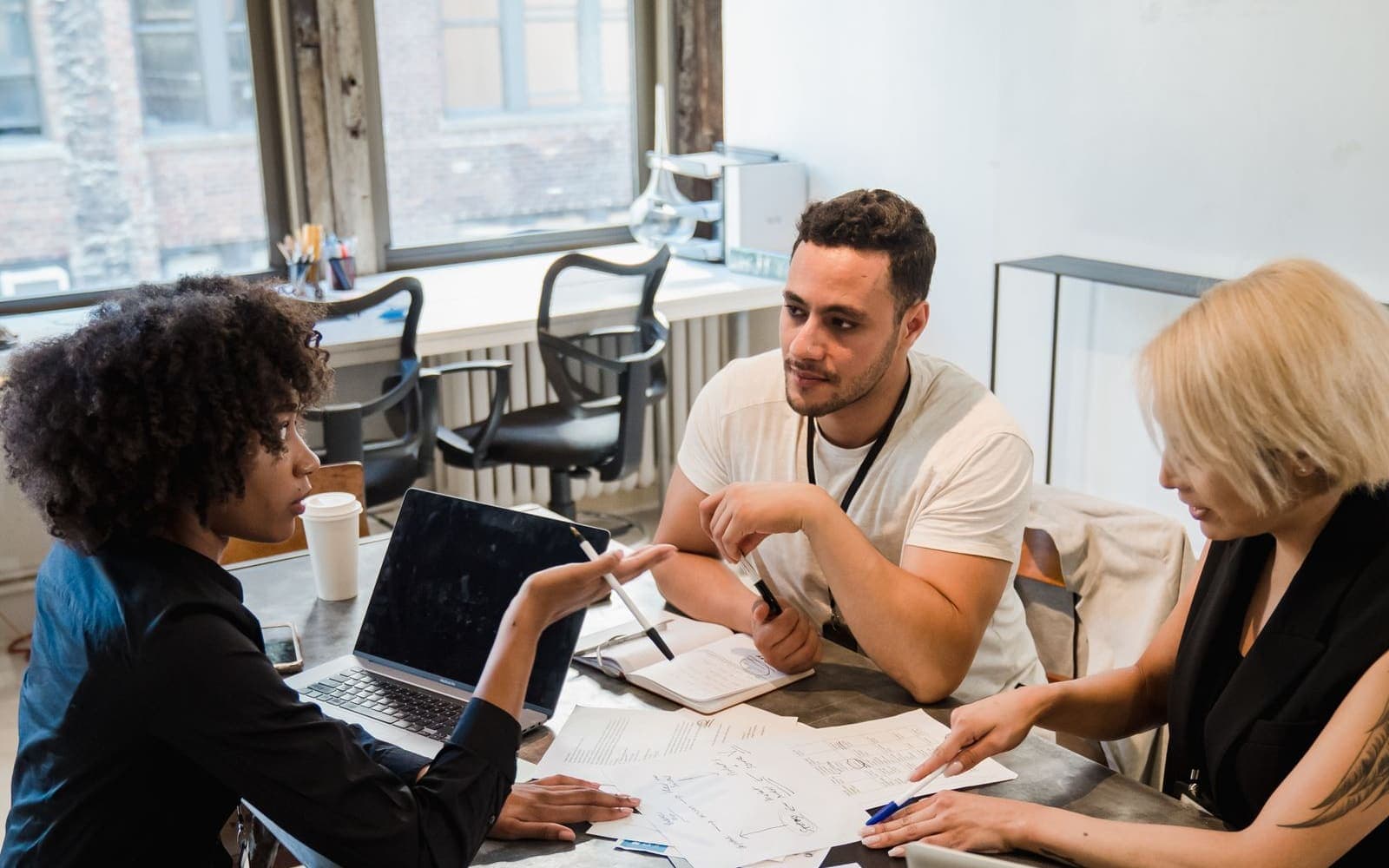 Three colleagues discussing sketches and a laptop in a studio