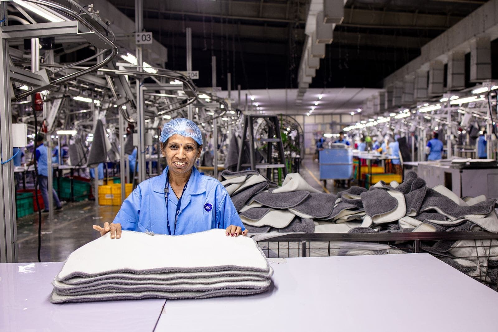 A textile factory worker at a table with the production floor behind