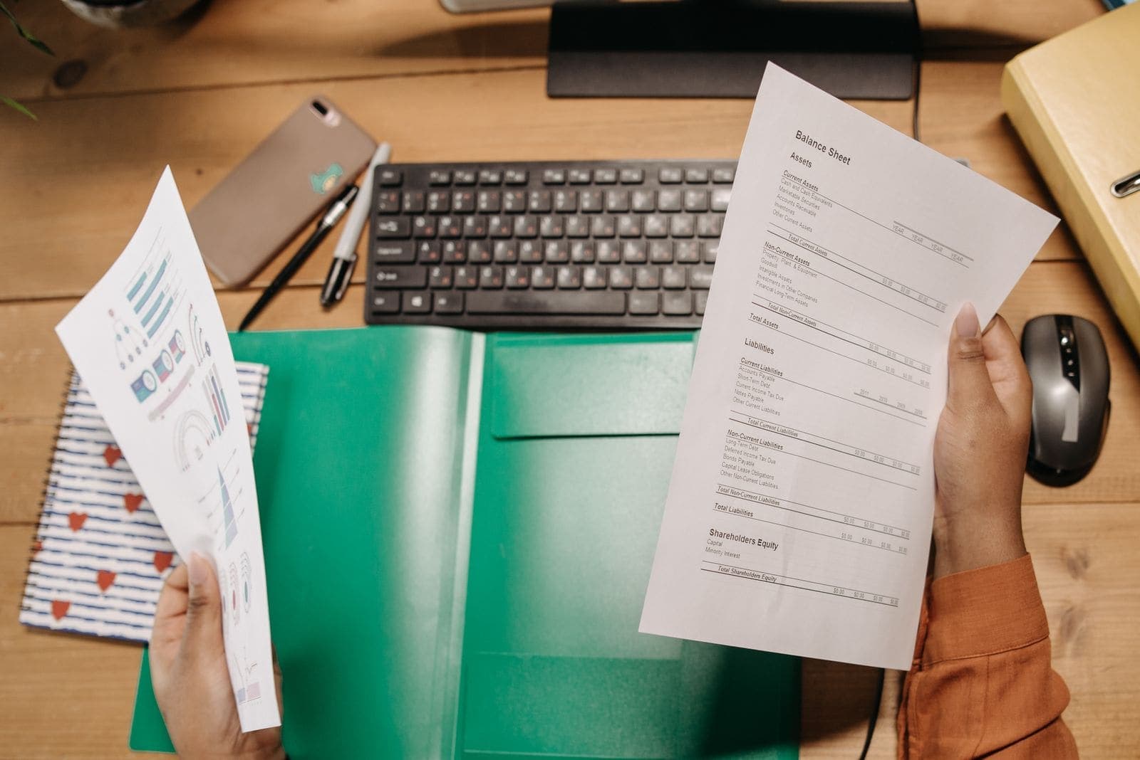 Hands holding a balance sheet and report over a desk
