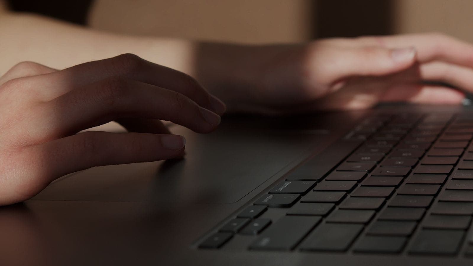 Hands typing on a laptop in dim light