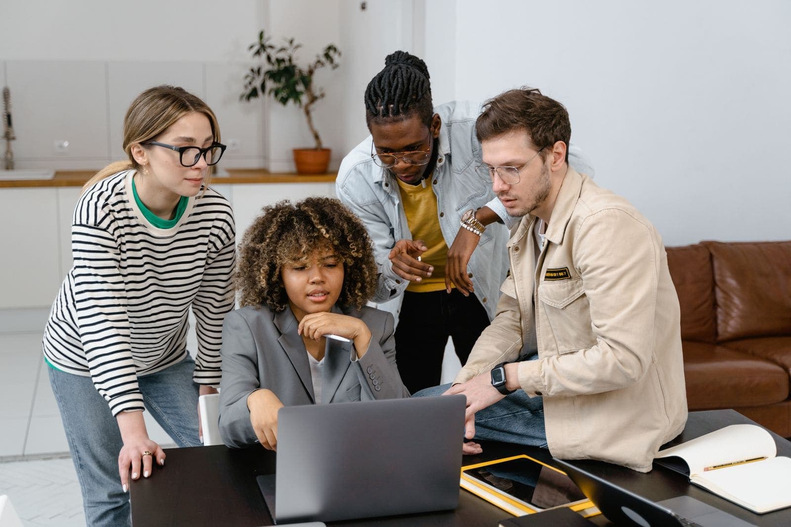 A team of four colleagues gathered around a laptop in a bright office